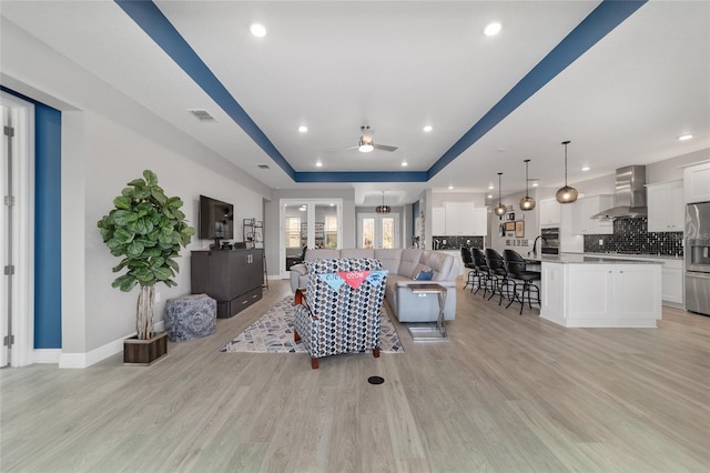 living room featuring a raised ceiling, ceiling fan, and light wood-type flooring