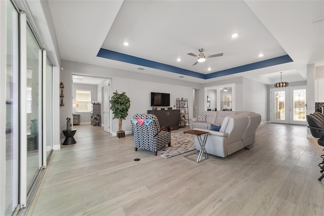 living room with a tray ceiling, ceiling fan, and light wood-type flooring