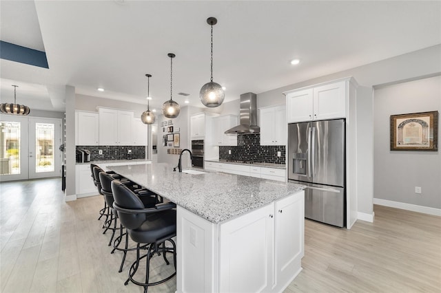 kitchen with white cabinets, appliances with stainless steel finishes, a center island with sink, and wall chimney range hood