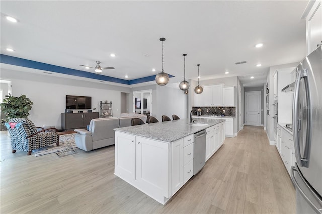 kitchen with light stone counters, stainless steel appliances, white cabinets, and a center island with sink