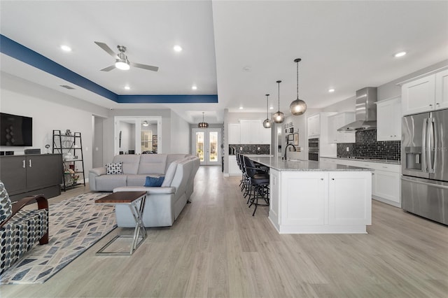 living room featuring ceiling fan, a tray ceiling, sink, and light hardwood / wood-style flooring