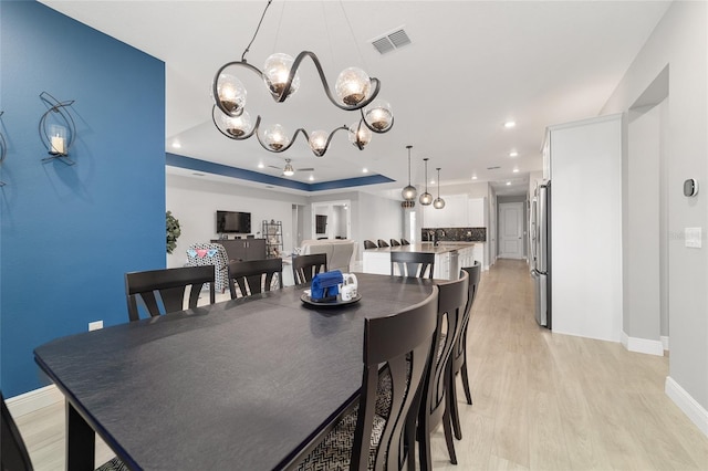 dining area with a raised ceiling, sink, a notable chandelier, and light wood-type flooring