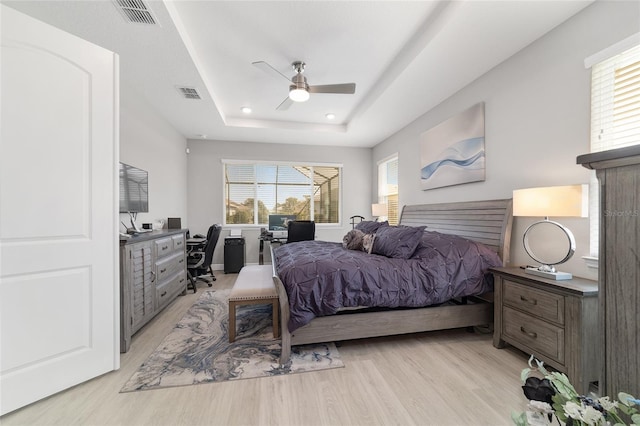 bedroom with ceiling fan, a raised ceiling, and light hardwood / wood-style floors