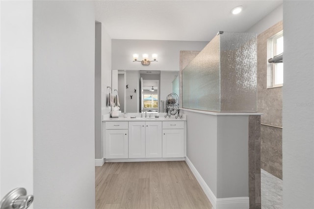 bathroom featuring a tile shower, vanity, and wood-type flooring