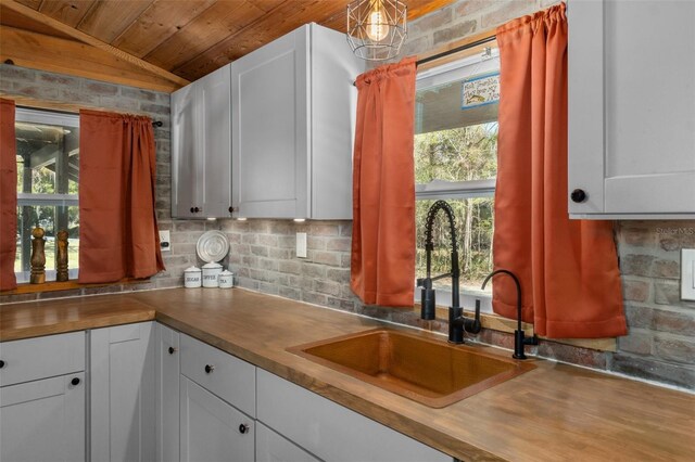 kitchen with tasteful backsplash, wooden ceiling, sink, and white cabinets