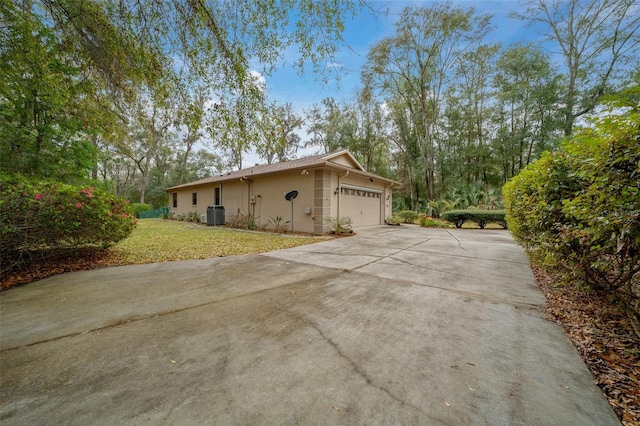 view of side of home featuring central AC unit, driveway, a yard, stucco siding, and a garage