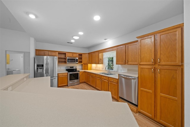 kitchen with light wood finished floors, open shelves, a sink, light countertops, and appliances with stainless steel finishes