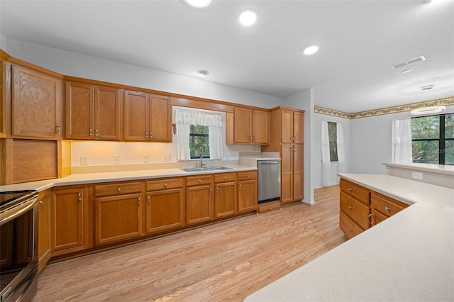 kitchen featuring brown cabinetry, stainless steel appliances, a sink, light countertops, and light wood-type flooring