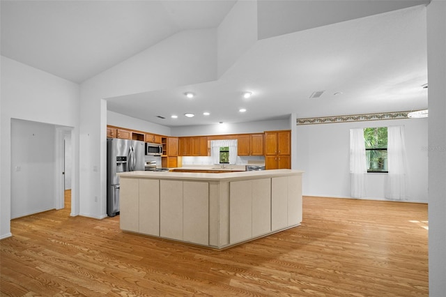 kitchen featuring light wood-type flooring, light countertops, vaulted ceiling, a wealth of natural light, and stainless steel appliances