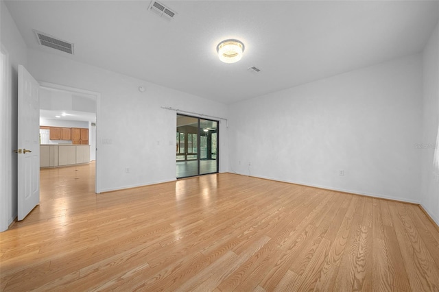 empty room with visible vents, light wood-type flooring, and baseboards