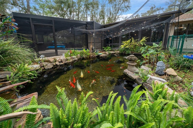 view of yard featuring a lanai, a swimming pool, fence, and a small pond