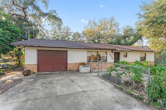 ranch-style home with stucco siding, fence, a garage, stone siding, and driveway