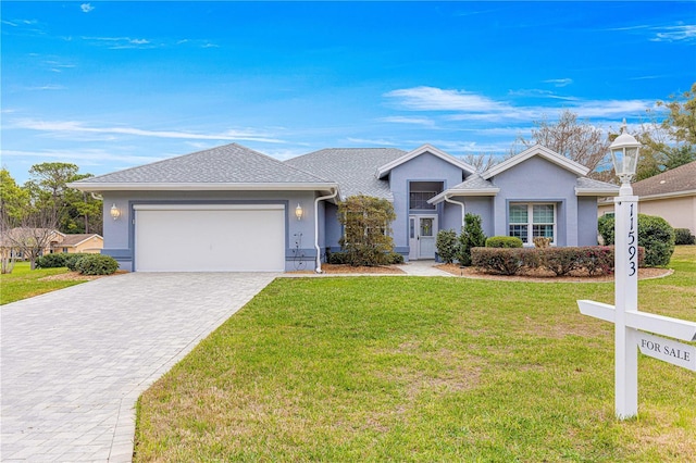 ranch-style house featuring a garage, a shingled roof, decorative driveway, stucco siding, and a front yard