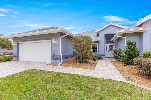 ranch-style home with decorative driveway, roof with shingles, stucco siding, a front yard, and a garage