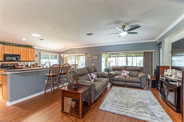 living room with a textured ceiling, hardwood / wood-style flooring, crown molding, and ceiling fan with notable chandelier