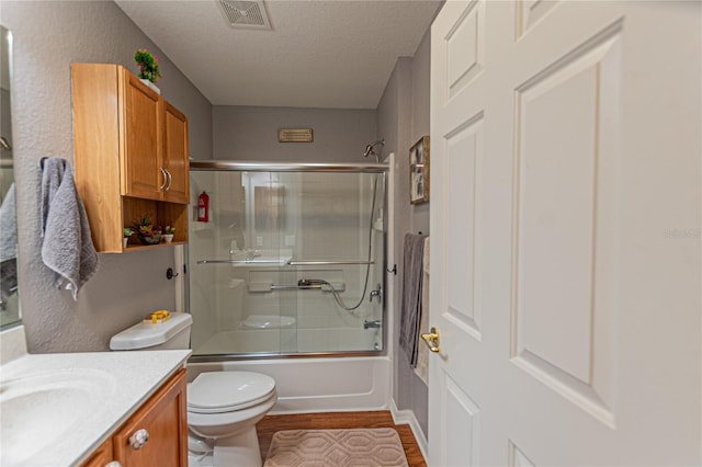 full bathroom with wood-type flooring, vanity, a textured ceiling, toilet, and bath / shower combo with glass door