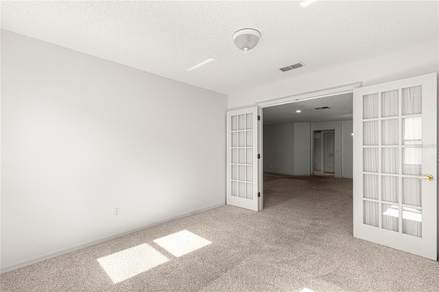 carpeted empty room with french doors, visible vents, and a textured ceiling