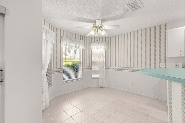 unfurnished dining area with visible vents, a ceiling fan, a textured ceiling, wallpapered walls, and baseboards