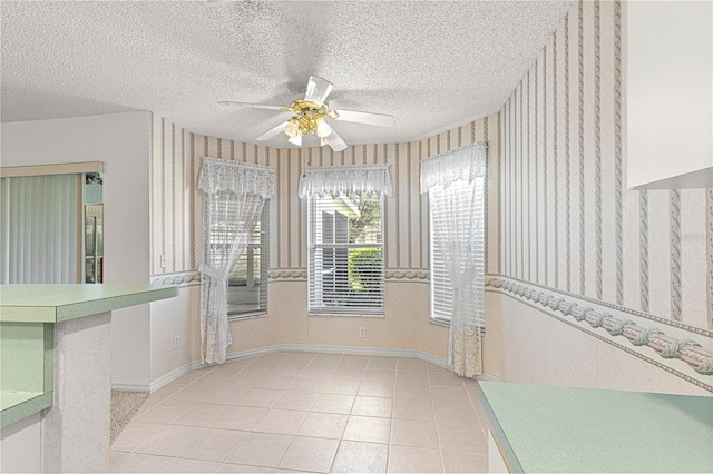 unfurnished dining area featuring wallpapered walls, baseboards, light tile patterned flooring, a textured ceiling, and a ceiling fan