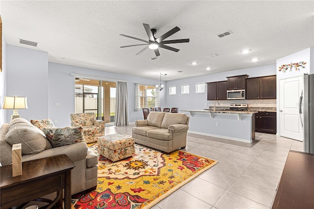 living room with sink, a textured ceiling, light tile patterned floors, and ceiling fan with notable chandelier