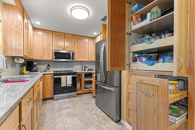 kitchen with appliances with stainless steel finishes, sink, tasteful backsplash, and light stone countertops