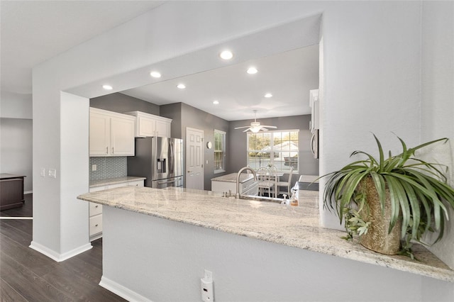 kitchen with sink, stainless steel fridge, kitchen peninsula, white cabinets, and light stone countertops