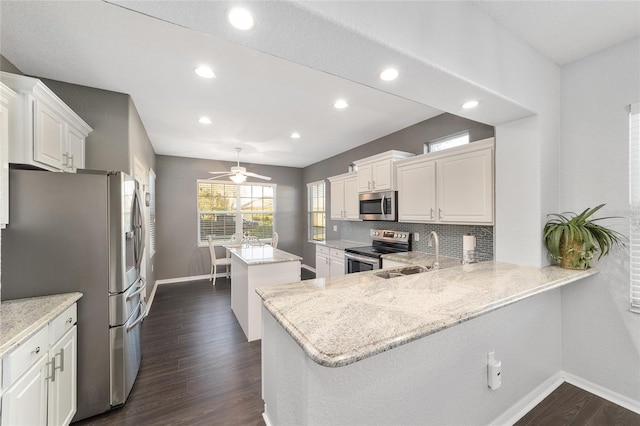 kitchen featuring sink, stainless steel appliances, kitchen peninsula, white cabinets, and light stone countertops