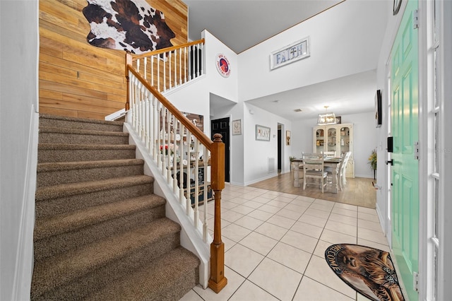 entryway featuring light tile patterned flooring, a high ceiling, wood walls, baseboards, and stairway