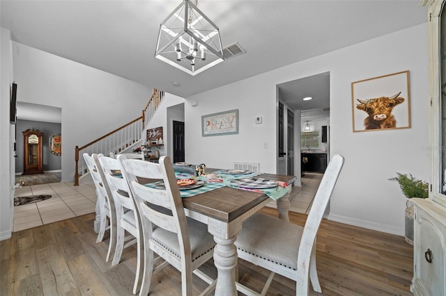 dining space featuring an inviting chandelier, stairs, visible vents, and wood finished floors