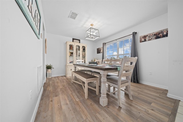 dining room with visible vents, light wood-style flooring, baseboards, and an inviting chandelier