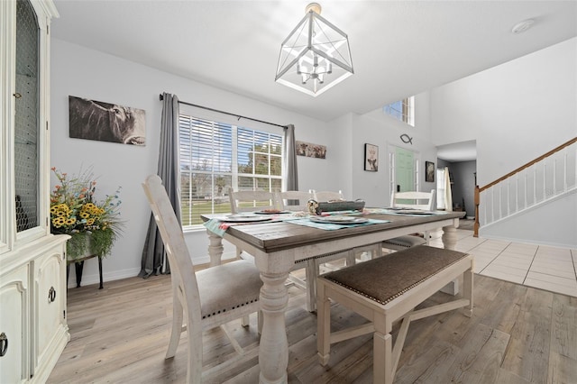 dining room featuring light wood-type flooring, a notable chandelier, baseboards, and stairs