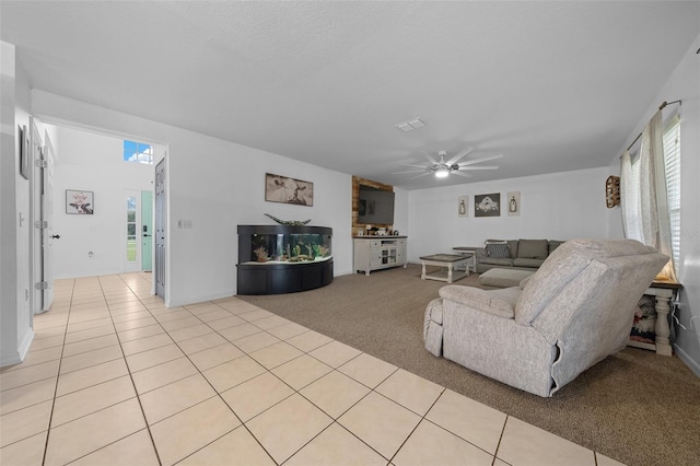 living area with light carpet, light tile patterned floors, visible vents, and a ceiling fan