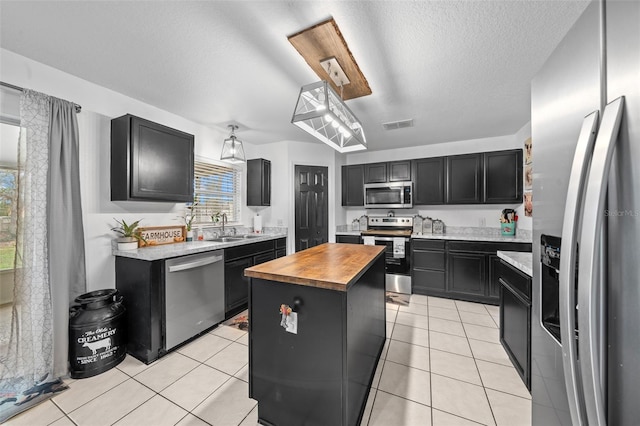 kitchen with light tile patterned floors, butcher block counters, appliances with stainless steel finishes, a center island, and dark cabinetry