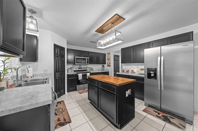 kitchen featuring dark cabinets, stainless steel appliances, a sink, a kitchen island, and decorative light fixtures