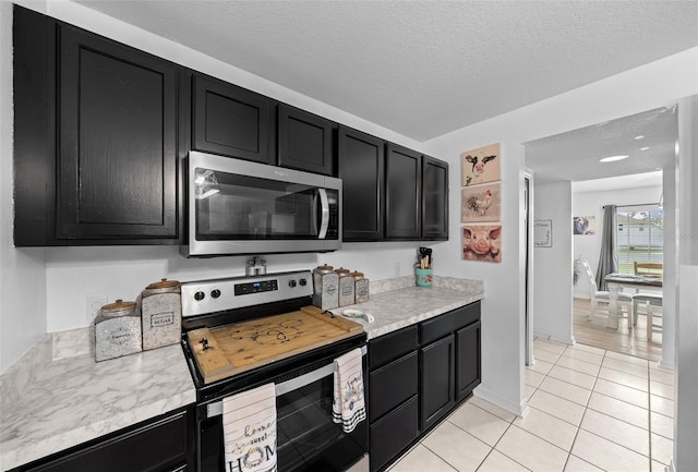 kitchen featuring light tile patterned floors, light countertops, appliances with stainless steel finishes, a textured ceiling, and dark cabinets