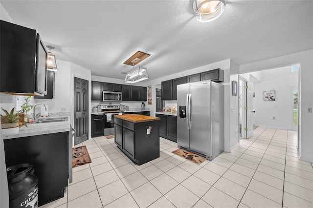 kitchen featuring butcher block countertops, appliances with stainless steel finishes, dark cabinets, a center island, and a sink