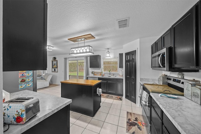 kitchen featuring a kitchen island, appliances with stainless steel finishes, dark cabinets, and butcher block countertops