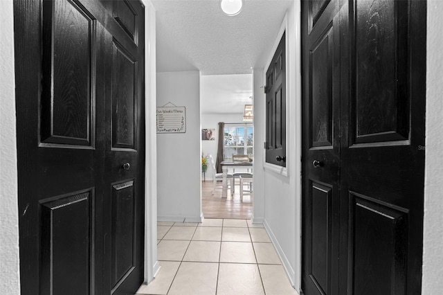 hallway featuring light tile patterned floors, a textured ceiling, and baseboards