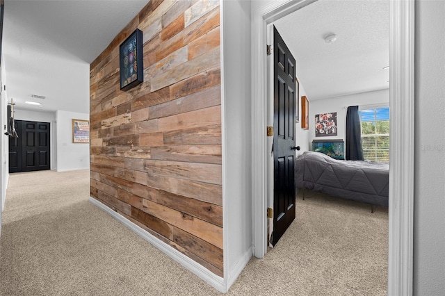 hallway featuring a textured ceiling, wood walls, visible vents, and light colored carpet