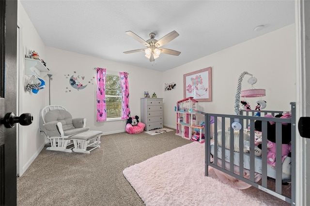 carpeted bedroom featuring ceiling fan, a crib, and baseboards