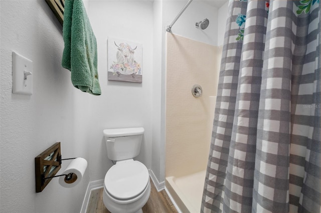 bathroom featuring a stall shower, wood finished floors, toilet, and baseboards