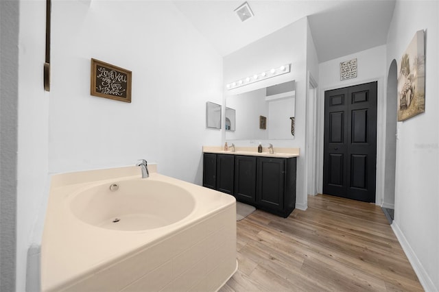 bathroom with double vanity, visible vents, a bath, wood finished floors, and a sink