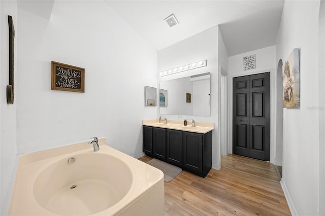 bathroom with double vanity, visible vents, wood finished floors, a garden tub, and a sink