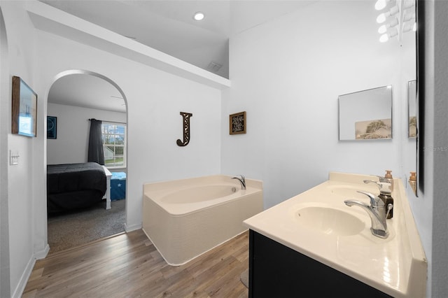 ensuite bathroom featuring a garden tub, double vanity, a sink, ensuite bath, and wood finished floors