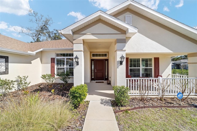 entrance to property with stucco siding, covered porch, and a shingled roof