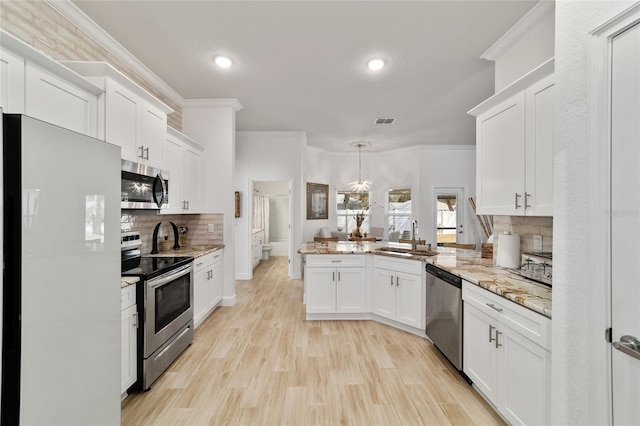 kitchen with stainless steel appliances, a peninsula, a sink, white cabinetry, and ornamental molding