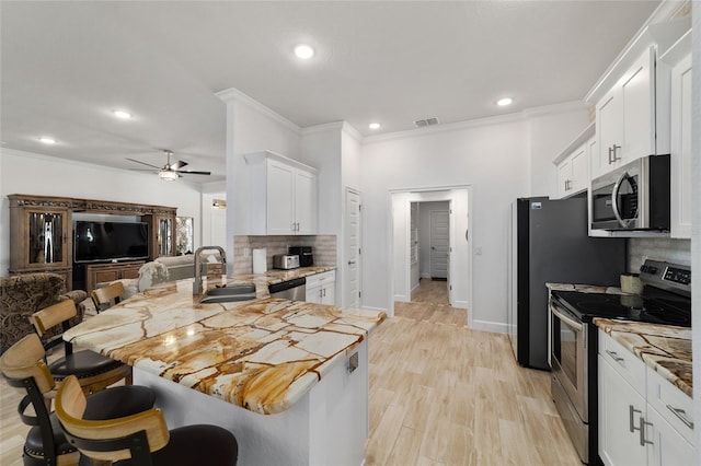 kitchen with appliances with stainless steel finishes, a breakfast bar, a peninsula, white cabinetry, and a sink