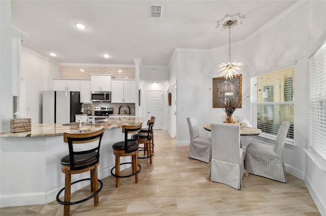 kitchen with visible vents, decorative backsplash, a kitchen breakfast bar, stainless steel appliances, and white cabinetry