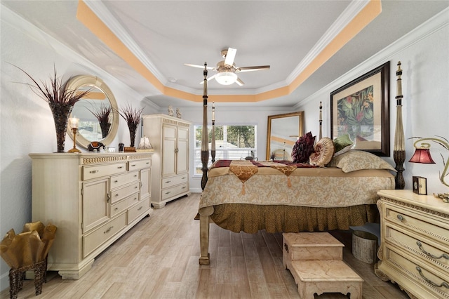 bedroom with light wood-type flooring, a tray ceiling, ornamental molding, and ceiling fan