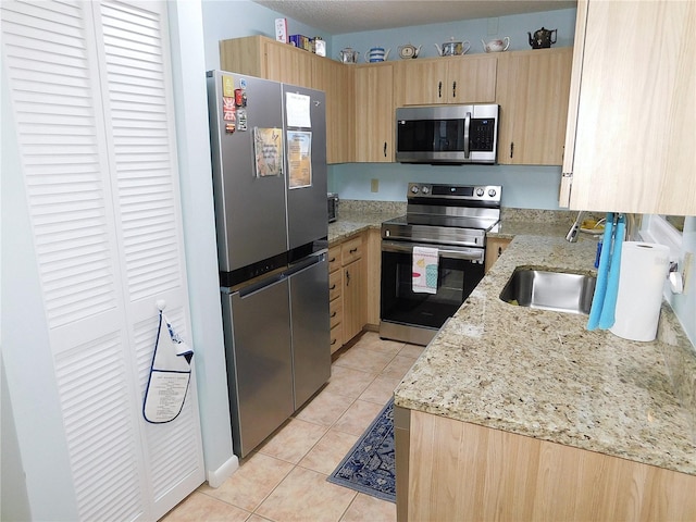 kitchen featuring stainless steel appliances, light stone countertops, sink, light tile patterned floors, and light brown cabinetry